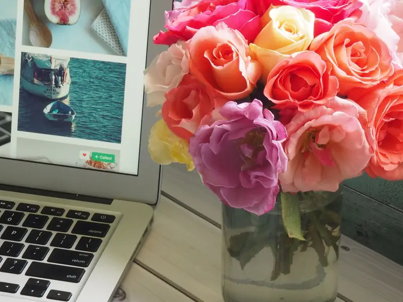 Open laptop on a white desk next to a bouquet of roses and magazines.