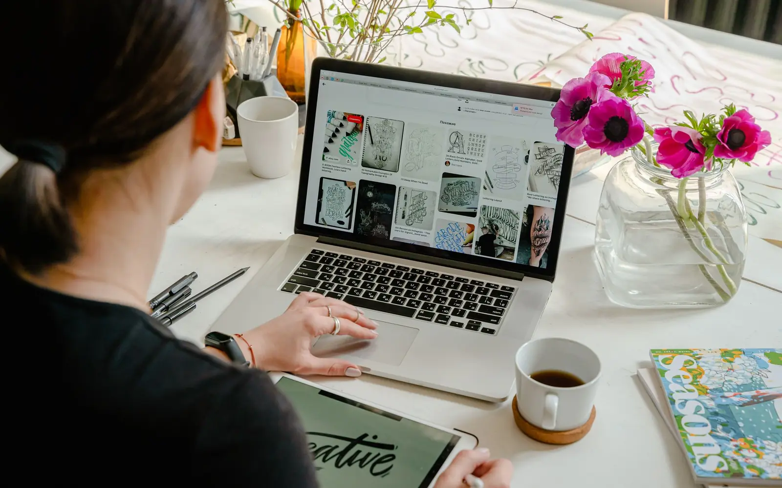 Creator browsing a grid of images on her laptop, next to a bouquet of pink flowers.